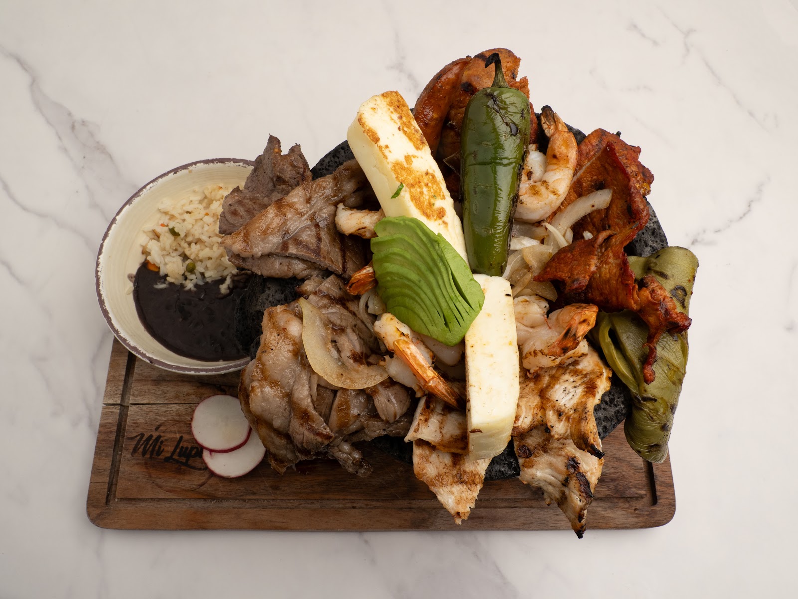 Molcajete — sizzling lava stone bowl with grilled meats and fresh salsas